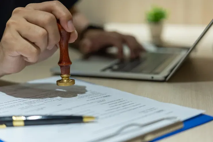 Hand stamping document near a laptop.